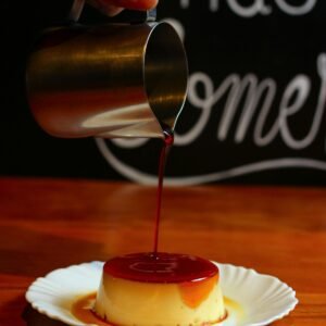 Hand pouring caramel sauce over a flan on a plate; close-up view, perfect for dessert presentations.